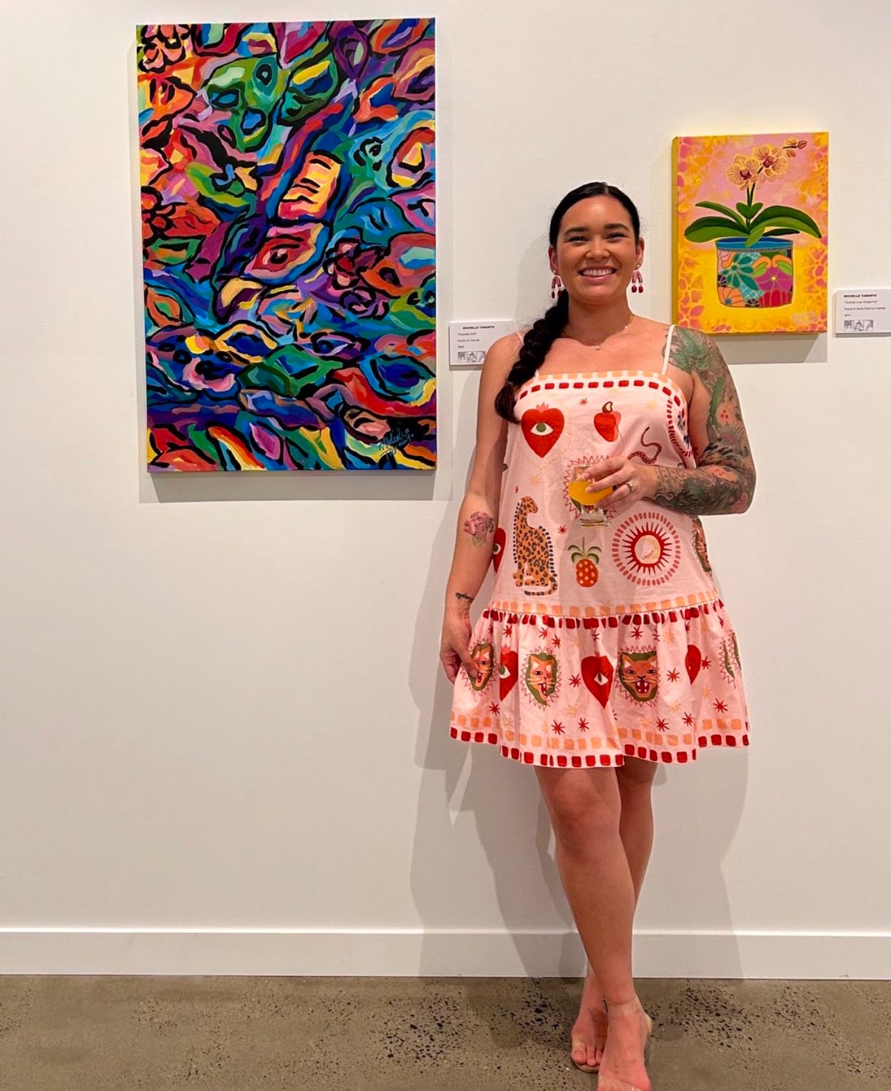 Woman in a patterned dress standing in front of colorful artwork at an art exhibition.